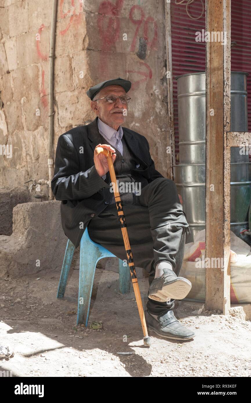 Uomo vecchio con un bastone da passeggio seduto su una sedia in plastica,  Mardin, Anatolia, Turchia orientale Foto stock - Alamy