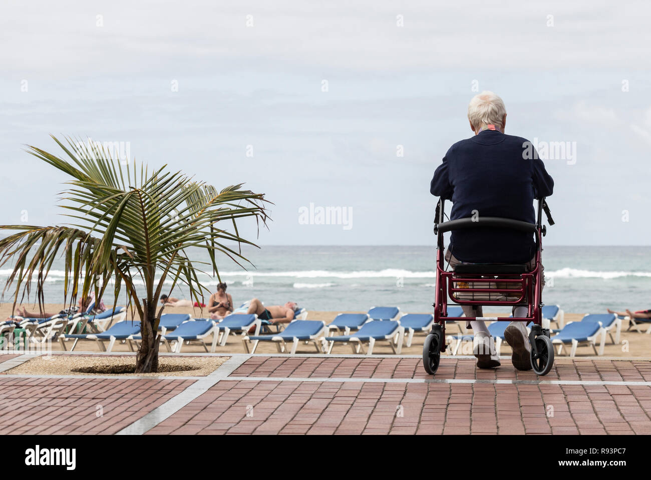 Uomo anziano siiting su walker affacciato sulla spiaggia in Spagna. Foto Stock