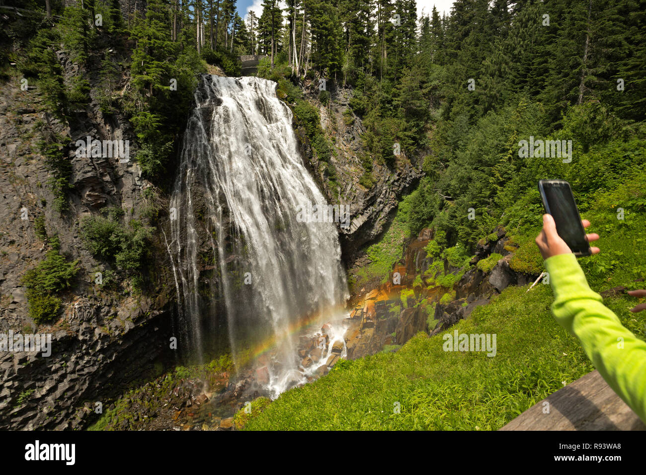 WA15592-00...WASHINGTON - Visitatore prendendo un telefono cellulare immagine dell'arcobaleno alla base di Narada cade sul fiume Paradiso in Mount Rainier Nazione Foto Stock