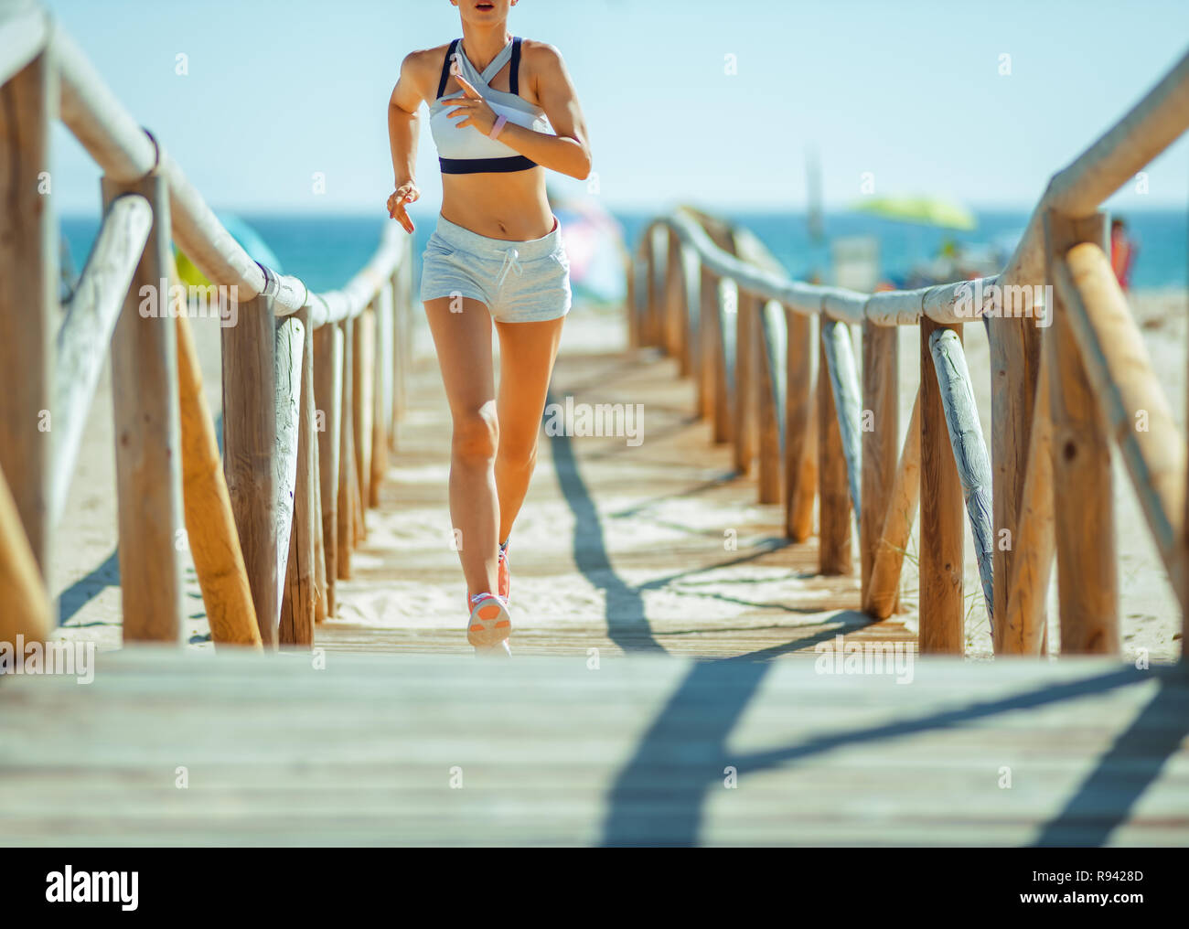 Primo piano sulla donna sana nel pareggiatore sport vestiti sulla costa dell'oceano in esecuzione. Rafforzare, aumentare la flessibilità e ridurre lo stress con la costa dell'oceano exc Foto Stock