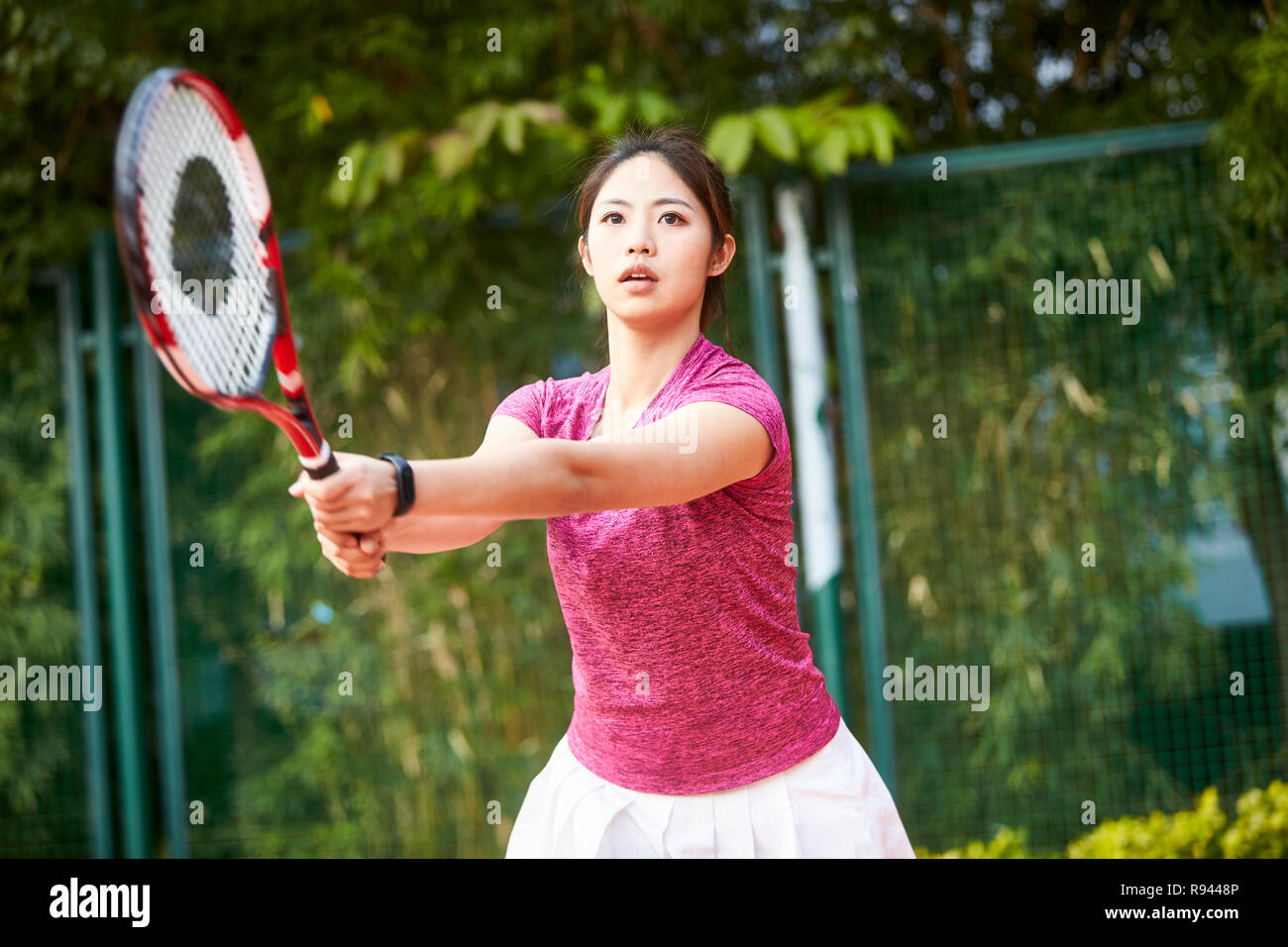 Giovane donna asiatica giocando a tennis all'aperto Foto Stock