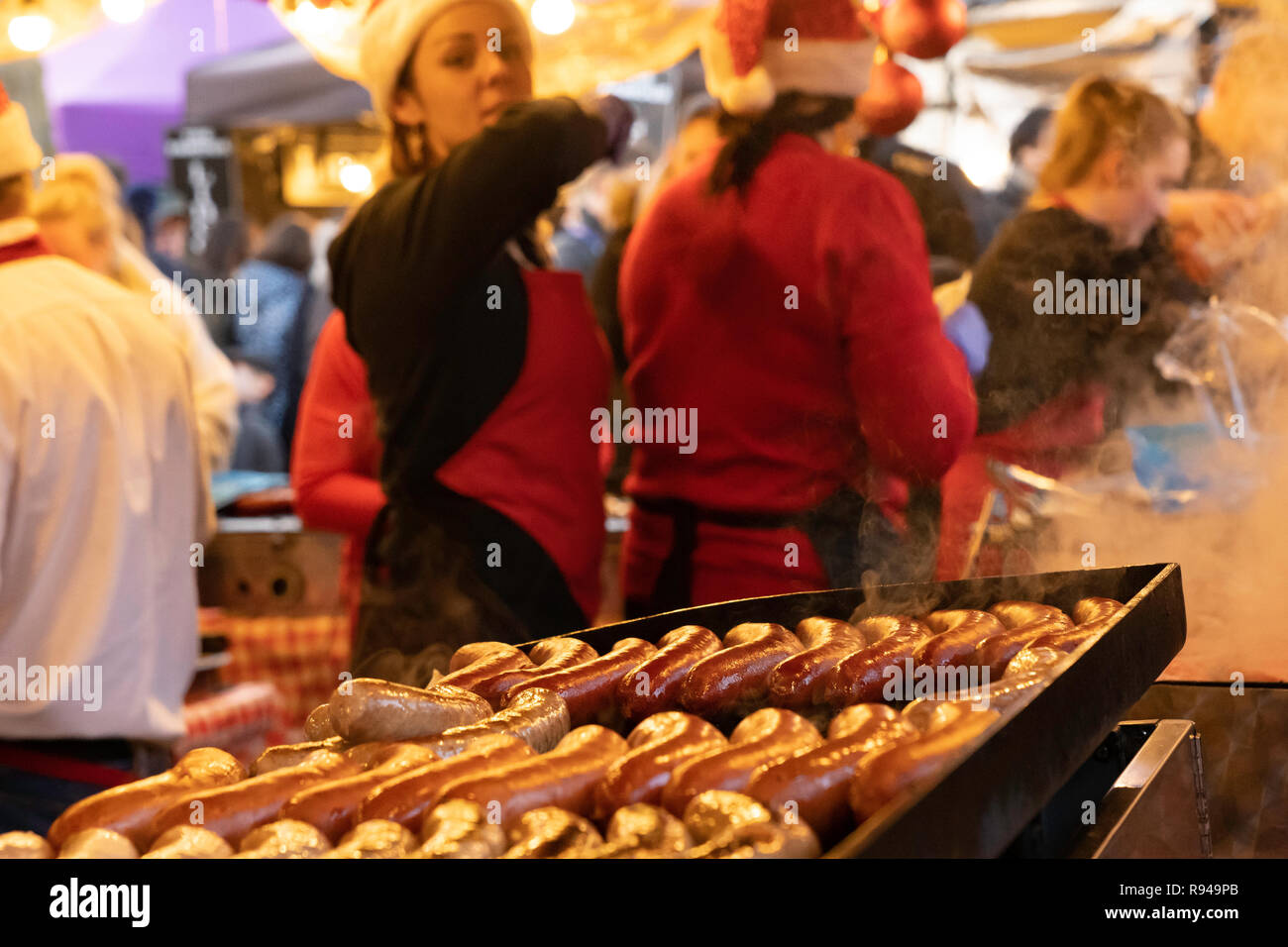 Sizzling salsicce cucina su un piatto caldo al mercato di Natale Harrogate, North Yorkshire, Inghilterra, Regno Unito. Foto Stock