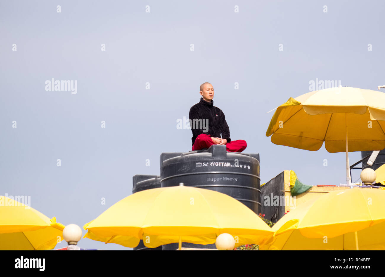 Buddista uomo meditando mentre seduto sulla parte superiore di un serbatoio di acqua sul tetto di un edificio in Kathmandu, Nepal Foto Stock