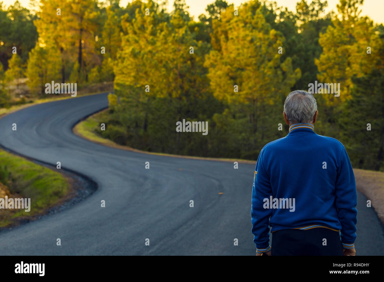 Active senior l uomo sta da solo sulla strada solitaria tra le montagne. Uomo più anziano di torna a camminare su lonely autostrada Foto Stock