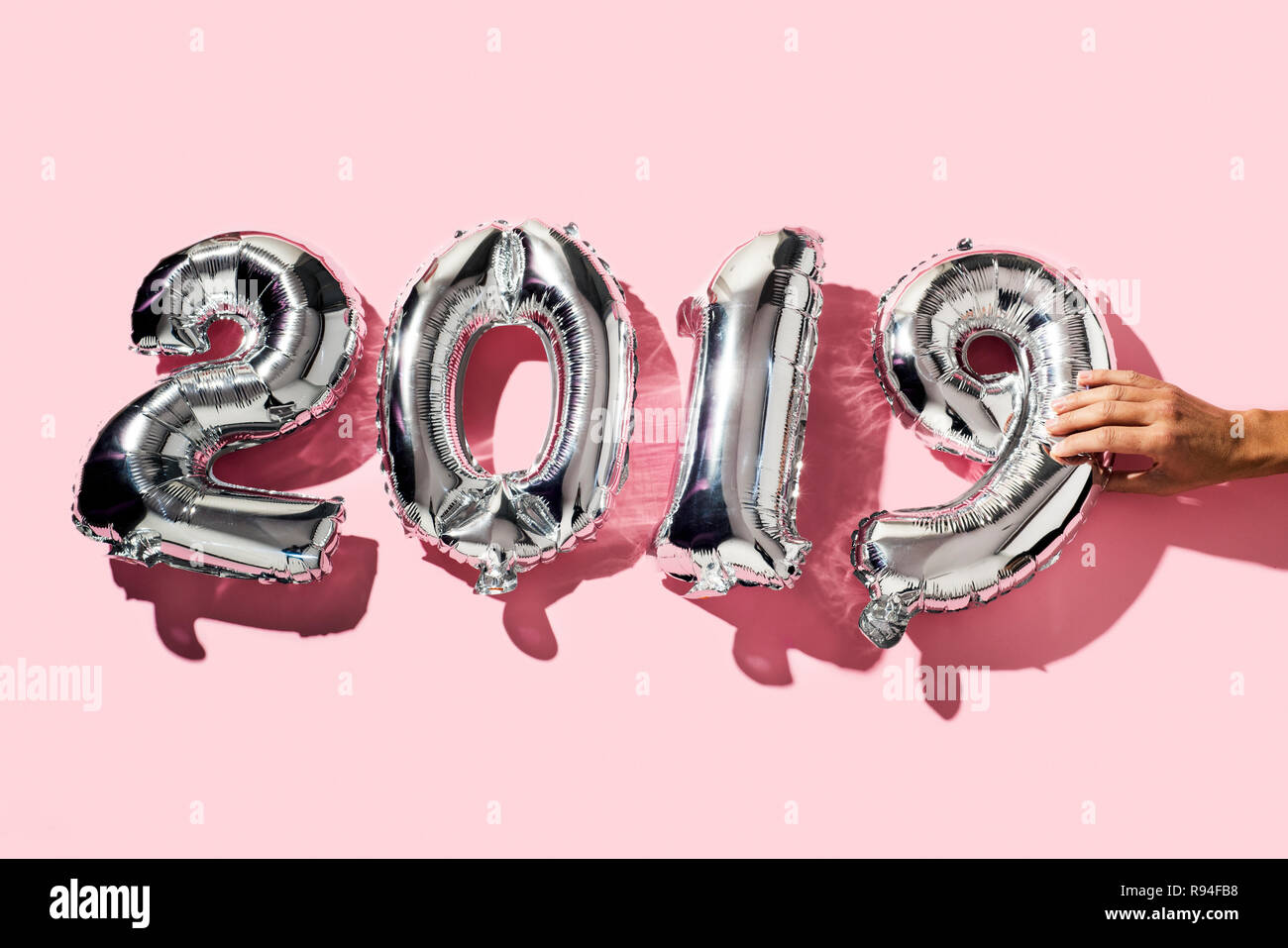 L'uomo formando il numero 2019, come il nuovo anno, un certo numero di argenteo di palloncini sagomati, su uno sfondo rosa Foto Stock