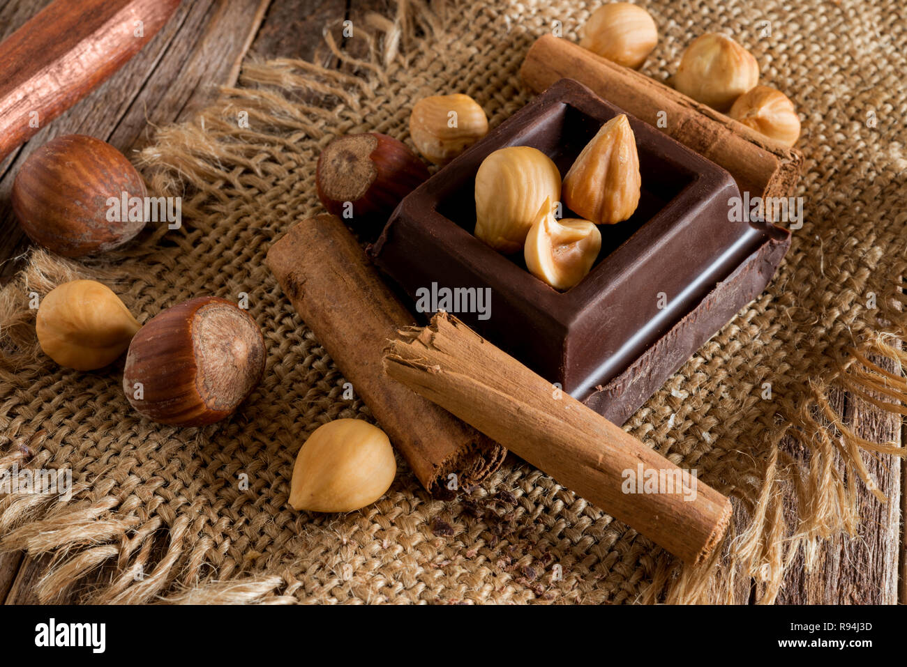 Blocco di cioccolato, nocciole sbucciate e cannella sul sacco di iuta sul tavolo di legno Foto Stock