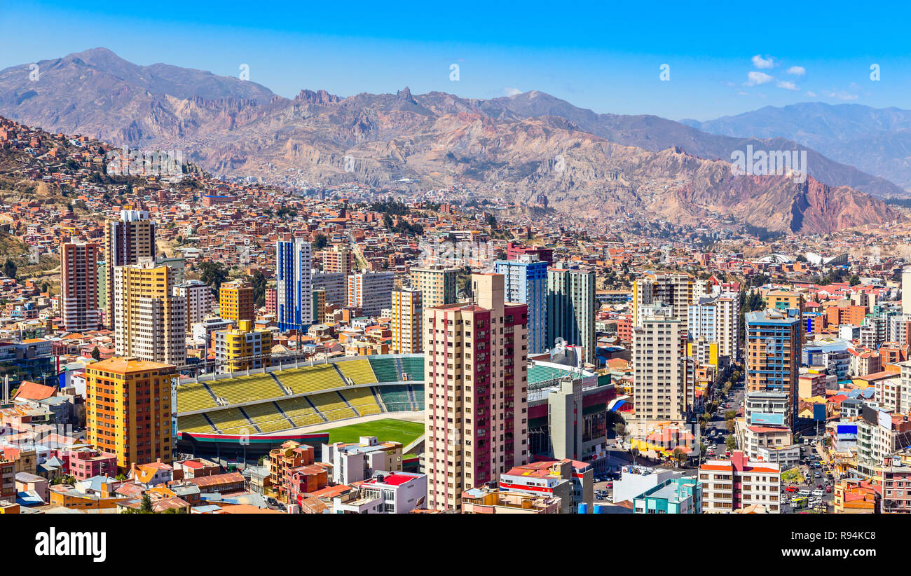 Nuestra Senora de la Paz colorata città centro città con grattacieli, stadio di calcio e un sacco di vita case sparse sulle colline con Andes mount Foto Stock