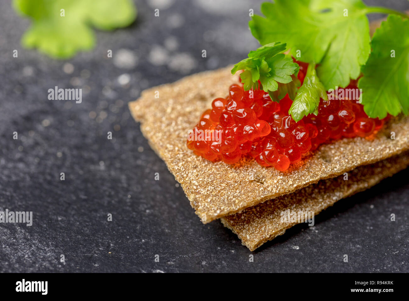 Fette biscottate di grano con caviale rosso e prezzemolo a sfondo nero. Gustoso sandwich, piatto natalizio Foto Stock