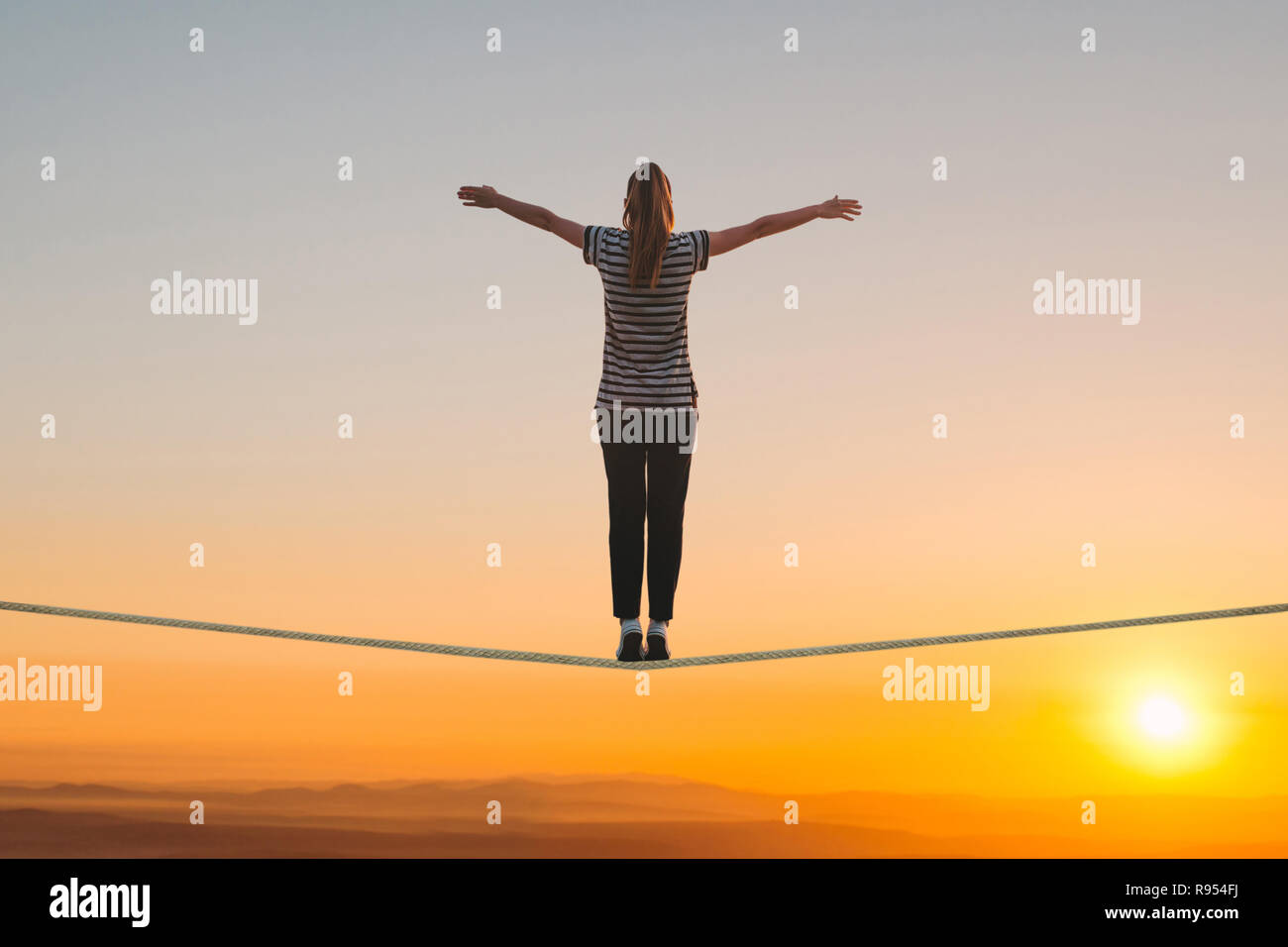 Una ragazza si erge sulla fune e solleva le mani contro il tramonto. Il concetto di libertà e di fiducia. Foto Stock