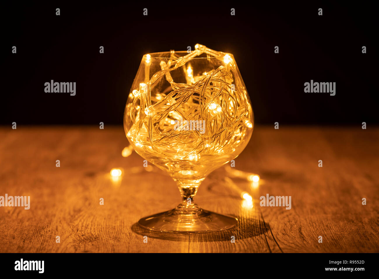 Il brandy di vetro con le luci fairy su un tavolo di legno Foto Stock