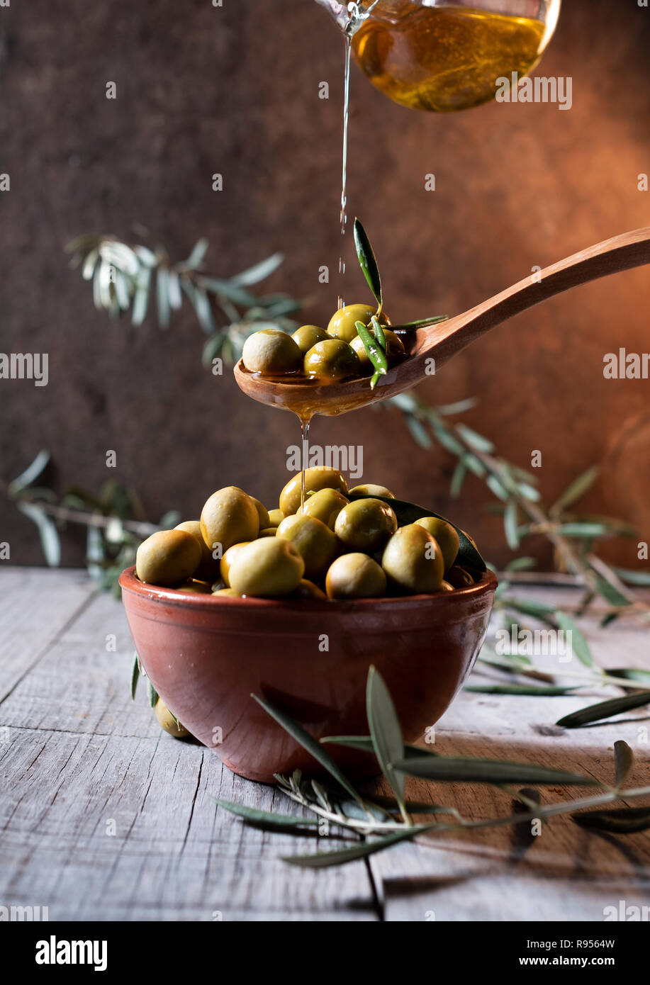 Olive in cucchiaio di legno versando olio sulla coppa Foto Stock