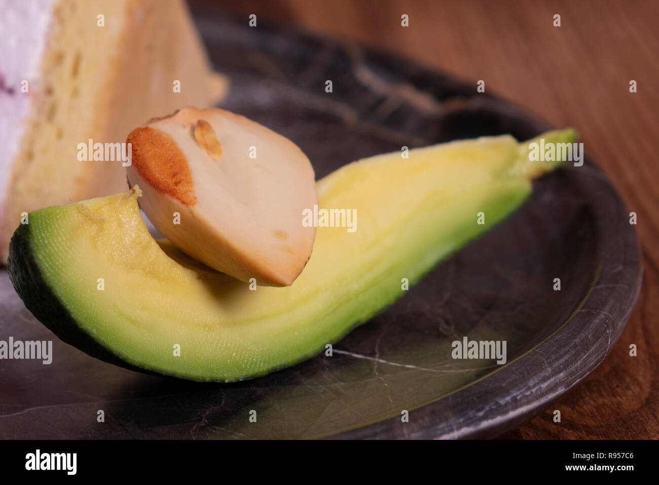 Avocado su piastra nera. Fette di avocado vista dall'alto in legno nero mature di sfondo verde e marrone Alligator Pear due metà di un seme. Le foglie di colore verde. Profes Foto Stock