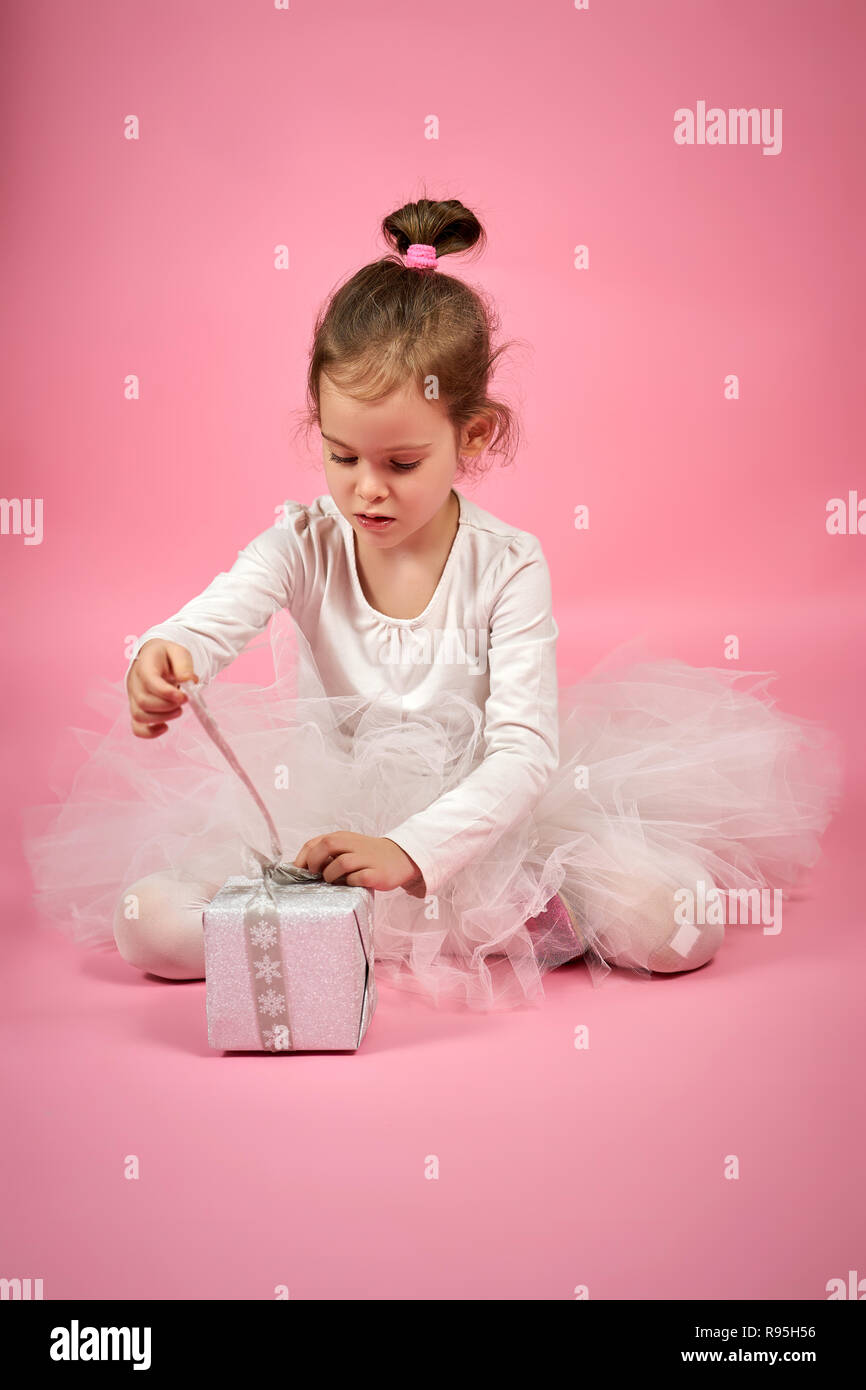 Carino bambina in tulle bianco mantello apre un regalo su un sfondo rosa Foto Stock