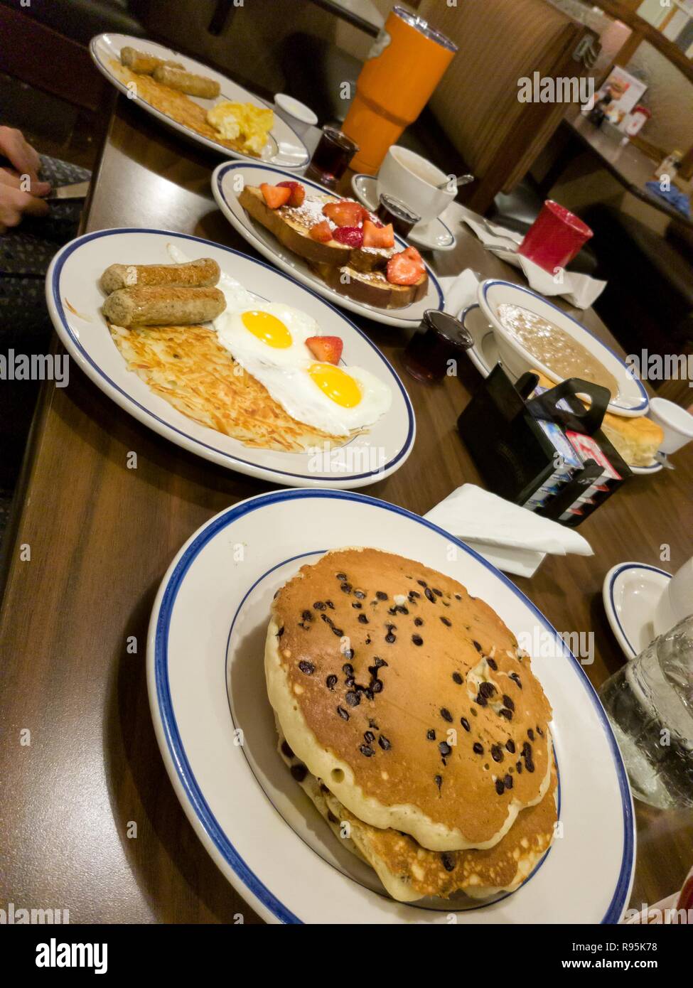 Tradizionale prima colazione americana al ristorante. Gocce di cioccolato frittelle, salsicce, soleggiato lato uova, hashbrows e toast francesi al ristorante. Pictu Foto Stock