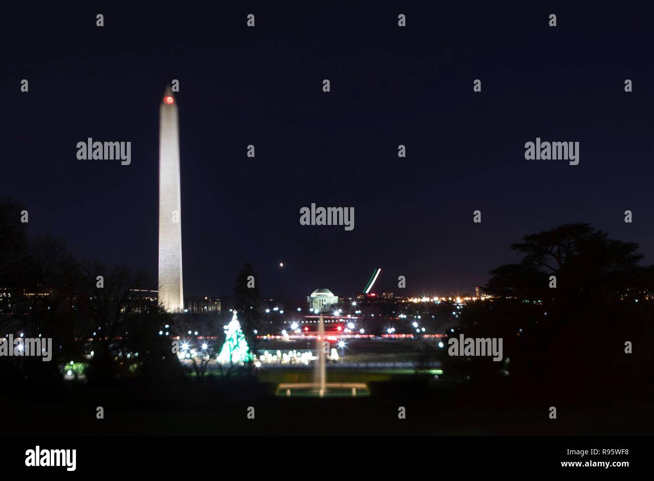Vista del Monumento a Washington e il National Mall dal South Lawn della Casa Bianca decorato per il Natale e illuminata di notte il 12 dicembre 2018 a Washington, DC. Le striature sono commerciali gli aerei che decollano dall'Aeroporto Nazionale Reagan sul Fiume Potomac. Foto Stock