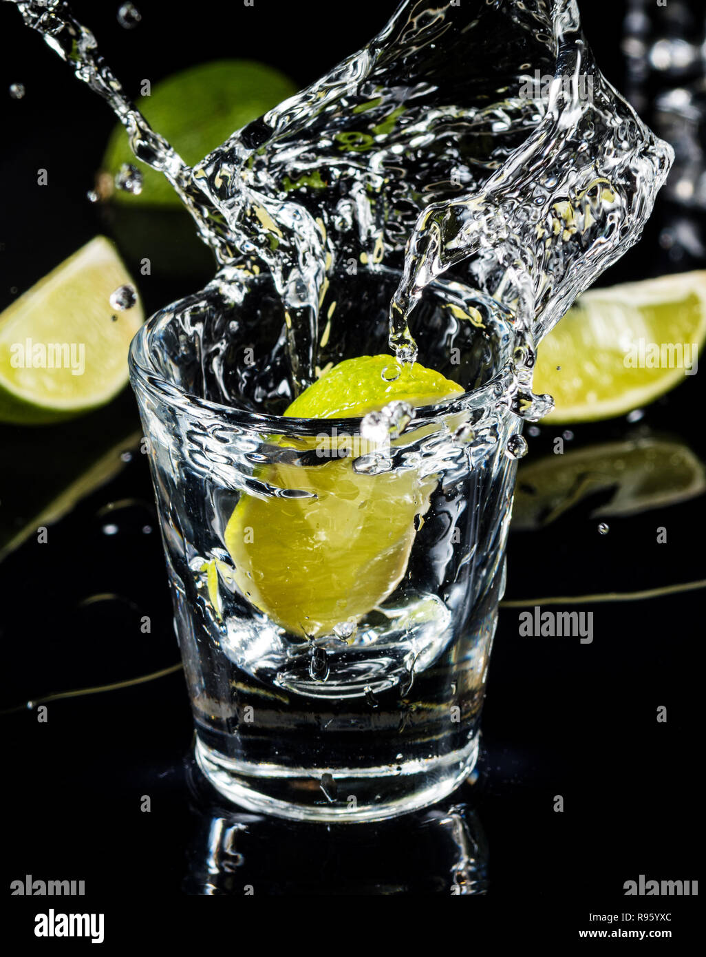 Tradizionale messicano Tequila splash lime su sfondo nero con il cubo del ghiaccio. Foto Stock