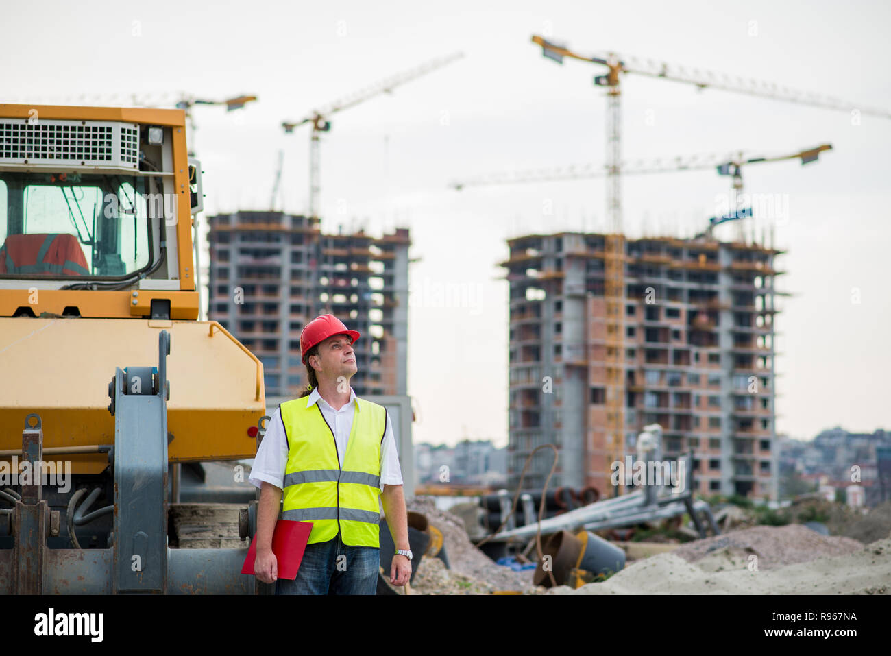 Ingegnere nella parte anteriore di escavatore su un sito di costruzione di edifici e la gru in background Foto Stock