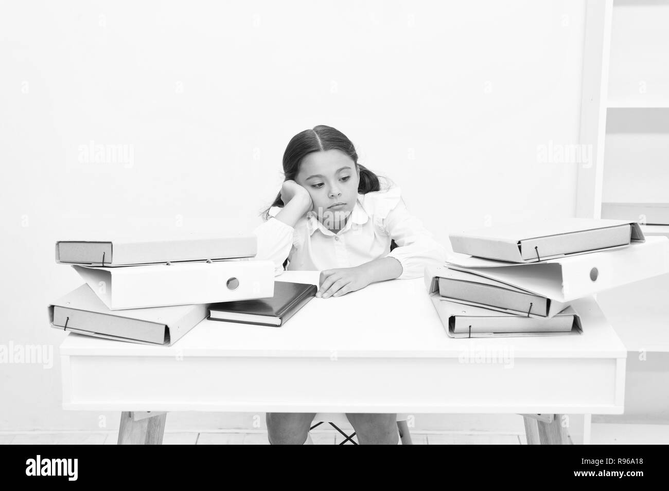 Troppo per imparare. Bambine stanco esaurito siedono al tavolo vicino a pila di libri sullo sfondo bianco. Schoolgirl stanchi di studiare e leggere libri. Kid uniformi scolastiche stanco faccia non desidera continuare la lettura. Foto Stock