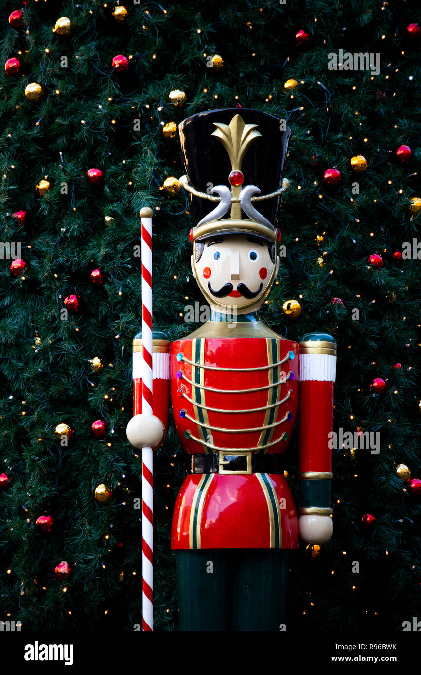 Centro città festosa display con il modello toy soldier su sentry in vintage cappotto rosso uniforme e albero di Natale con luci dietro Foto Stock