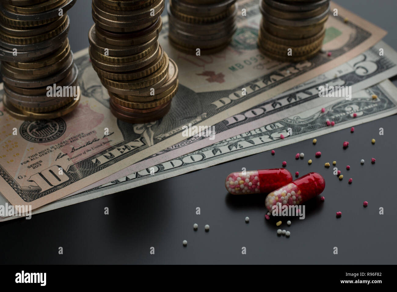 Pillole o capsule con contenuti sparsi e le fatture del dollaro, pile di monete sullo sfondo. Concetto di trattamento costoso Foto Stock