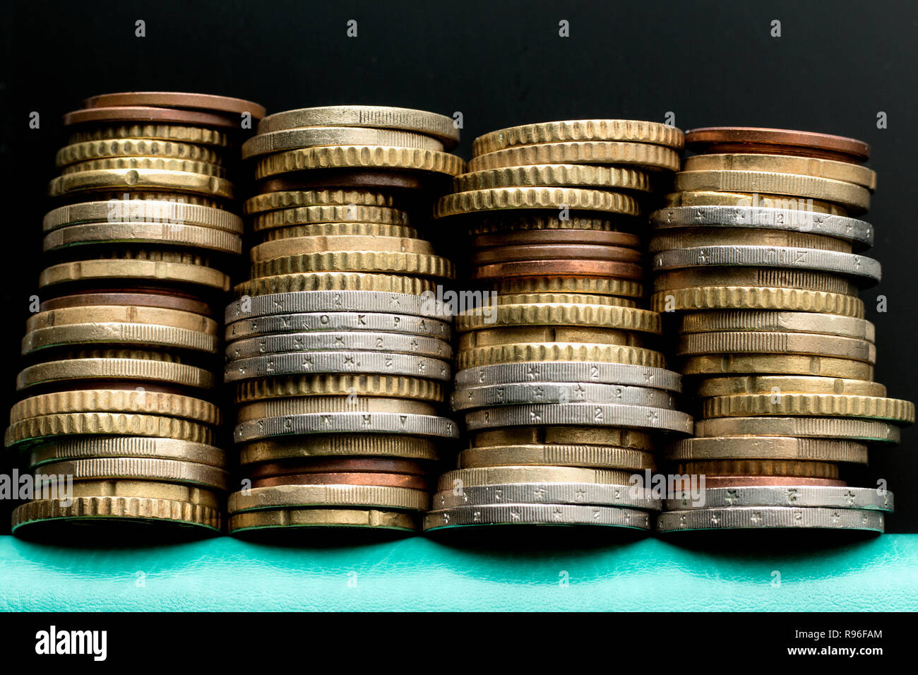 Quattro pile di monete in euro sul turchese del notebook su sfondo nero. Per argomenti economia, bilancio familiare, risparmi Foto Stock