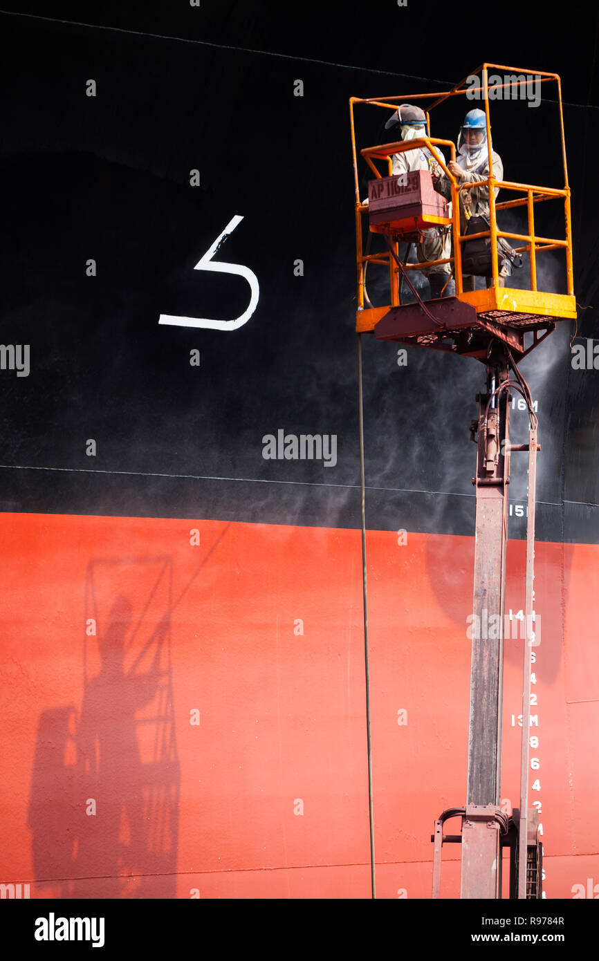 Due lavoratori su una navicella hydroblasting la superficie di uno scafo di imbarcazione per la manutenzione. Foto Stock