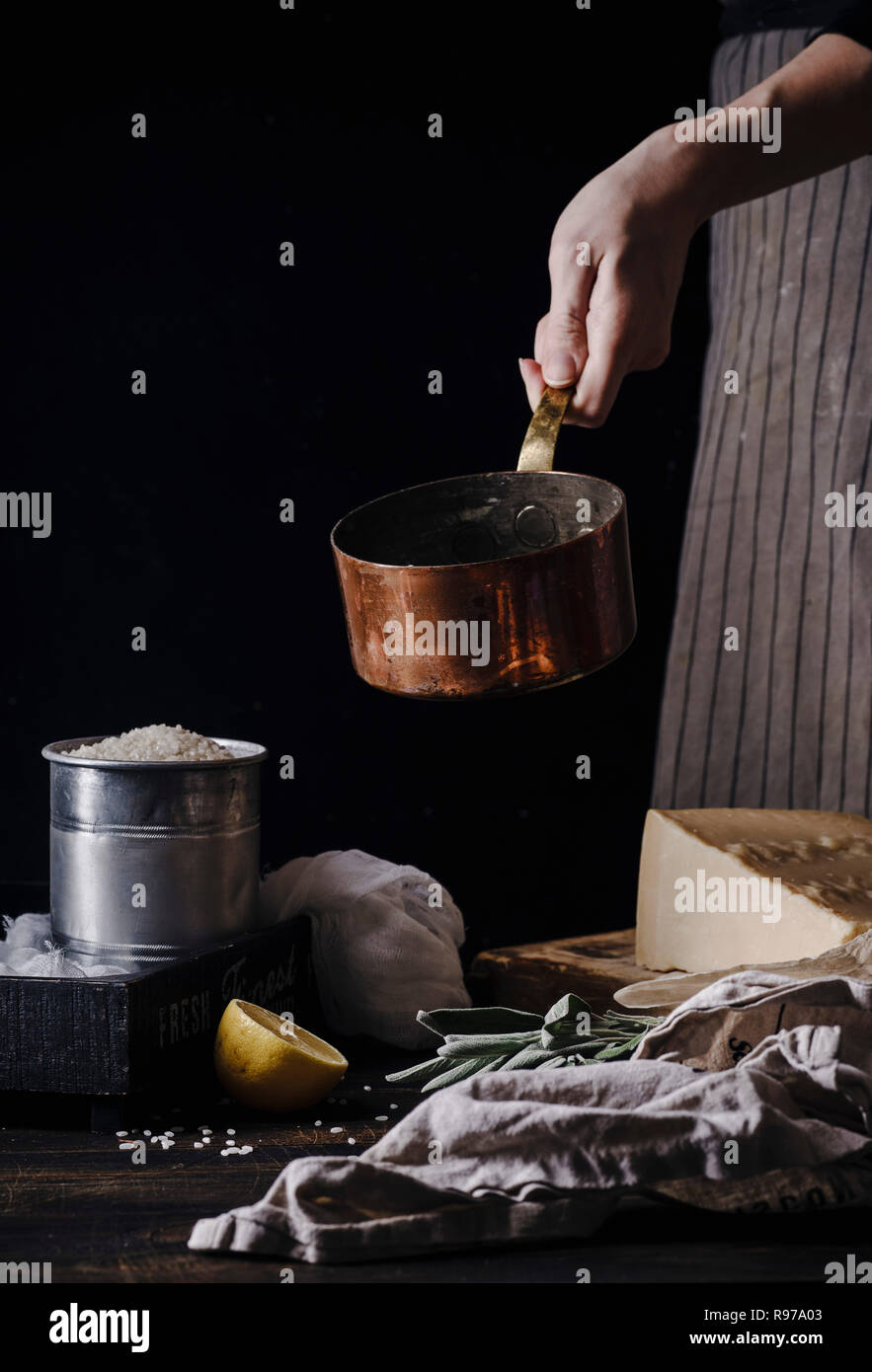 Mani femminili per la cottura risotto. Pentola di Rame, riso, parmigiano  ingredienti. Sfondo scuro Foto stock - Alamy