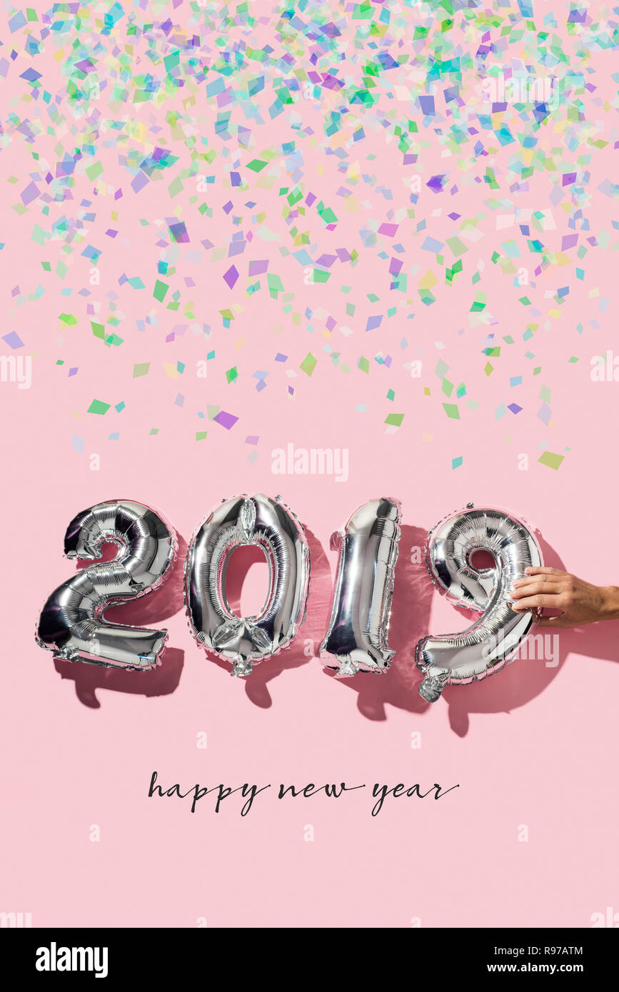 Alcuni coriandoli, un uomo formando il numero 2019, come il nuovo anno, con qualche numero argenteo a forma di palloncini e il testo felice anno nuovo su una rosa backgrou Foto Stock