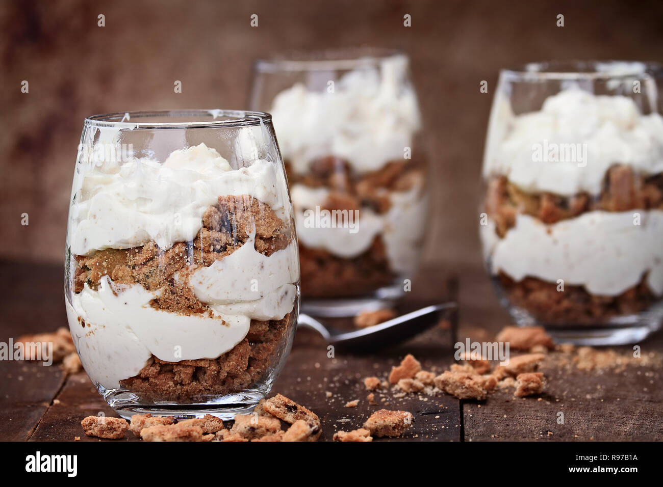 Tre Bicchieri di sbriciolato biscotti con scaglie di cioccolato e cheesecake parfaits contro un sfondo rustico. Estrema profondità di campo con fo selettiva Foto Stock