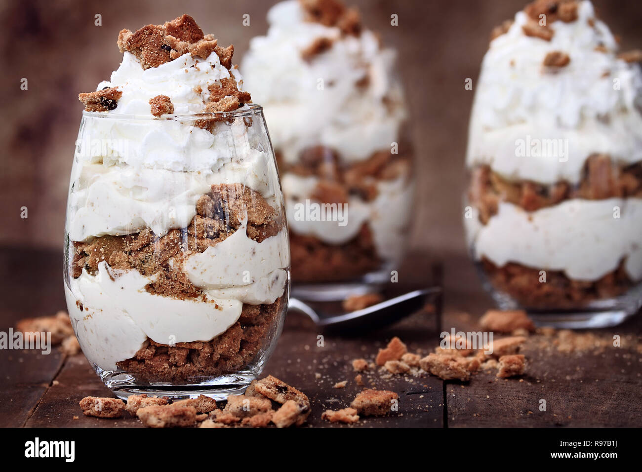 Tre Bicchieri di sbriciolato biscotti con scaglie di cioccolato e cheesecake parfaits contro un sfondo rustico. Estrema profondità di campo con fo selettiva Foto Stock