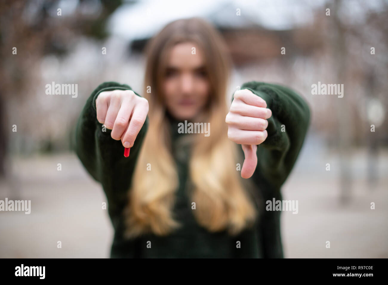Sfocato giovane femmina mostra piccoli red medicina e gesticolando il pollice verso il basso rimanendo in posizione di parcheggio Foto Stock