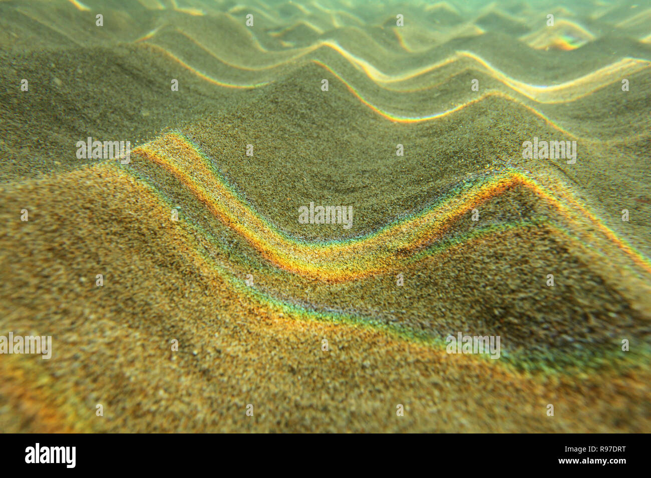 Fotografia subacquea - luce rifratta sulla superficie del mare formando arcobaleni sulla sabbia di piccole dimensioni 'dunes' in acqua poco profonda vicino alla spiaggia. Abstract sfondo marino. Foto Stock
