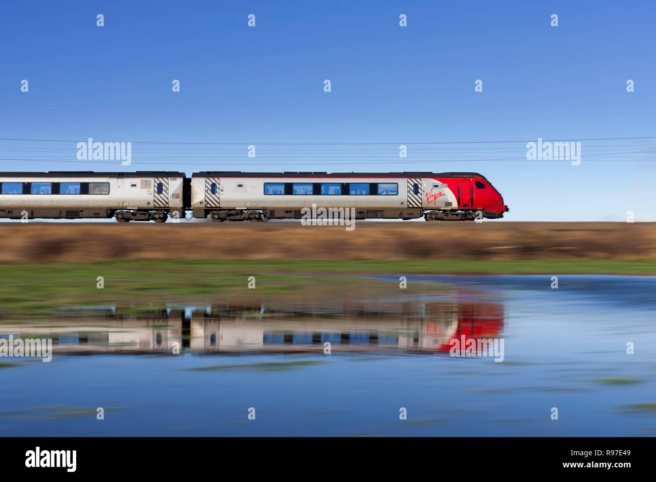 Un Virgin Trains classe 221 voyager treno diesel accelerando lungo la linea principale della costa occidentale si riflette in un campo inondato Foto Stock