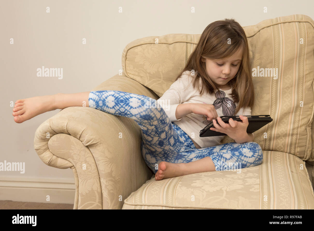 Ragazza giovane la posa di un divano a giocare con un iPad, un dispositivo digitale, tablet, media elettronici, social media, sei-anno-vecchio. Foto Stock
