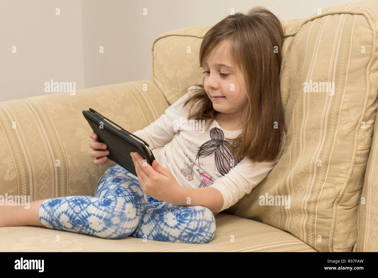 Ragazza giovane la posa di un divano a giocare con un iPad, un dispositivo digitale, tablet, media elettronici, social media, sei-anno-vecchio. Foto Stock