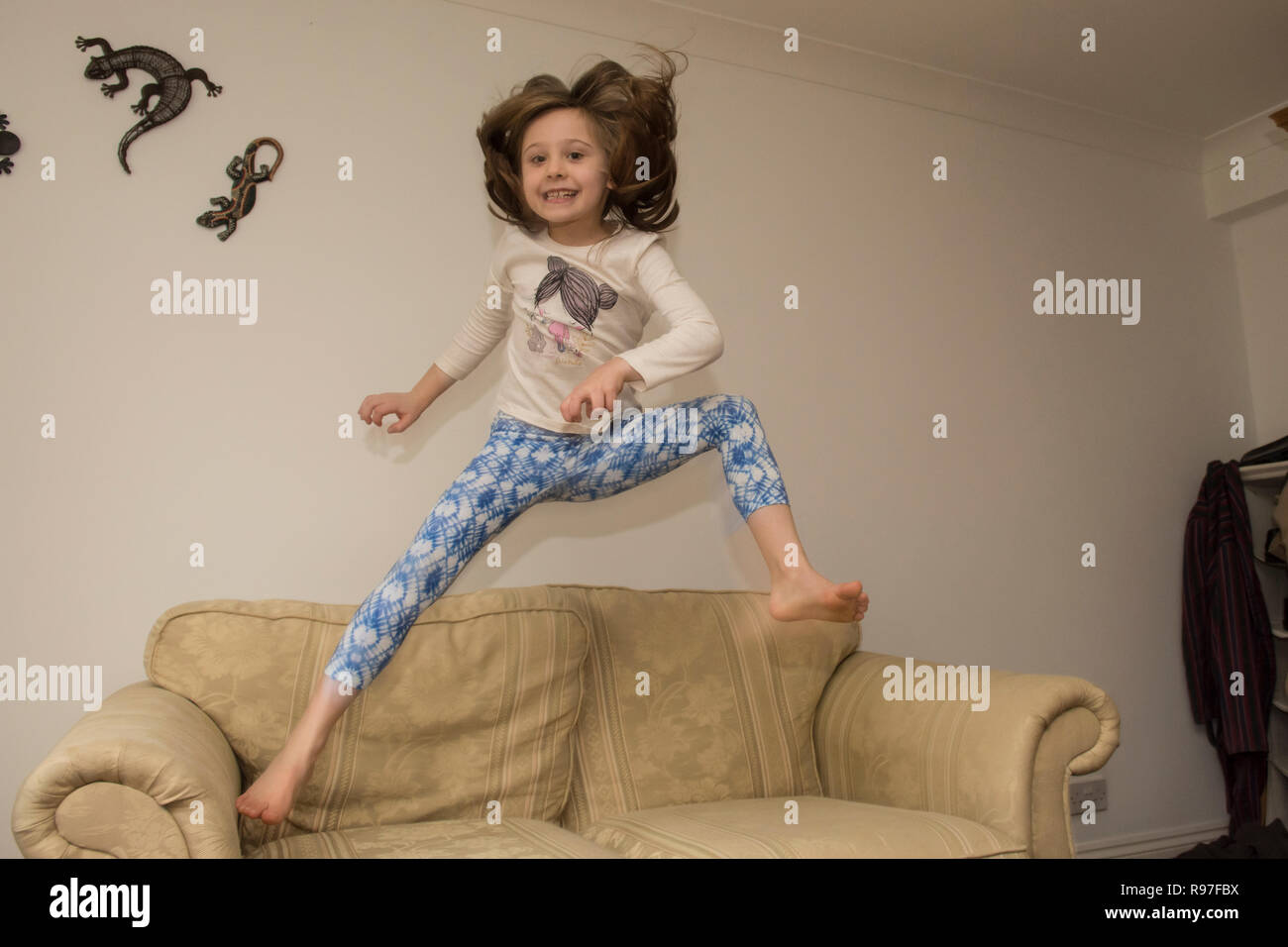 Bambino, ragazza in interni che saltava, saltando su mobili, divano, essendo energico, iperattivo, divertendosi, sei anni, Foto Stock