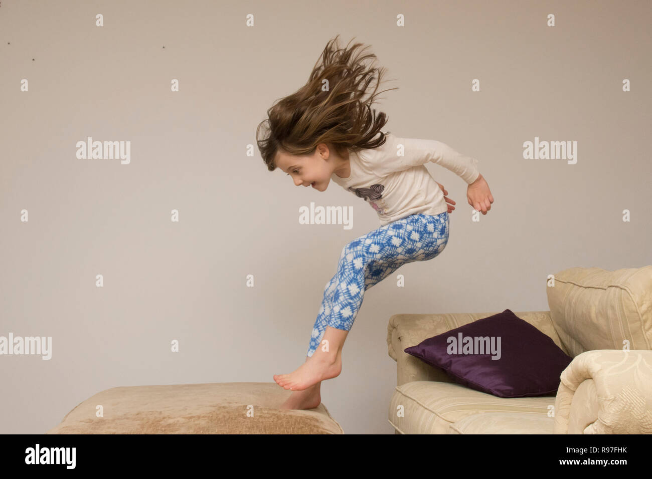 Bambino, ragazza in interni che saltava, saltando su mobili, divano, essendo energico, iperattivo, divertendosi, sei anni, Foto Stock