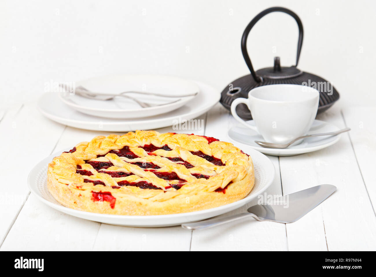 Berry crostata con ciliegie e lamponi su bianco tavolo in legno. Cup, sottovasi e teiera su sfondo sfocato. Foto Stock