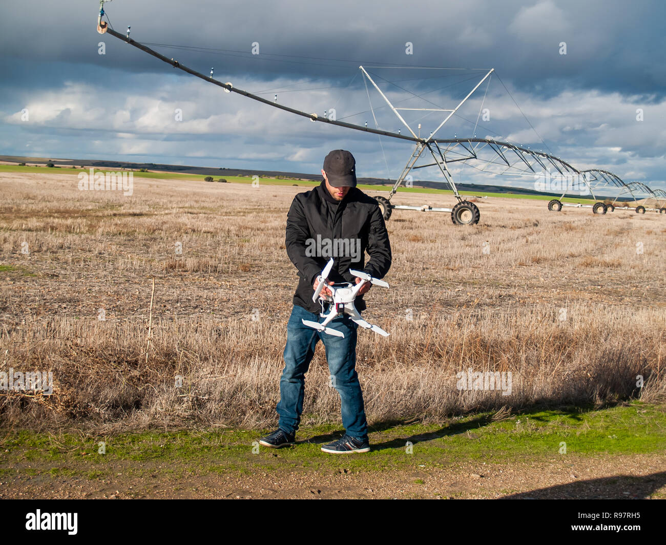 Un drone pilota configurando il suo drone in un campo con e sistema di irrigazione prima del volo Foto Stock