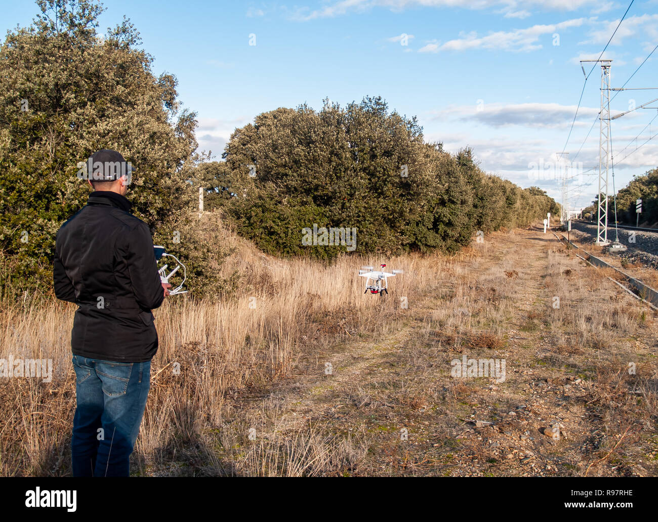 Un drone di pilotaggio pilota con il telecomando con lo smartphone nelle sue mani nella foresta vicino alla stazione del treno Foto Stock