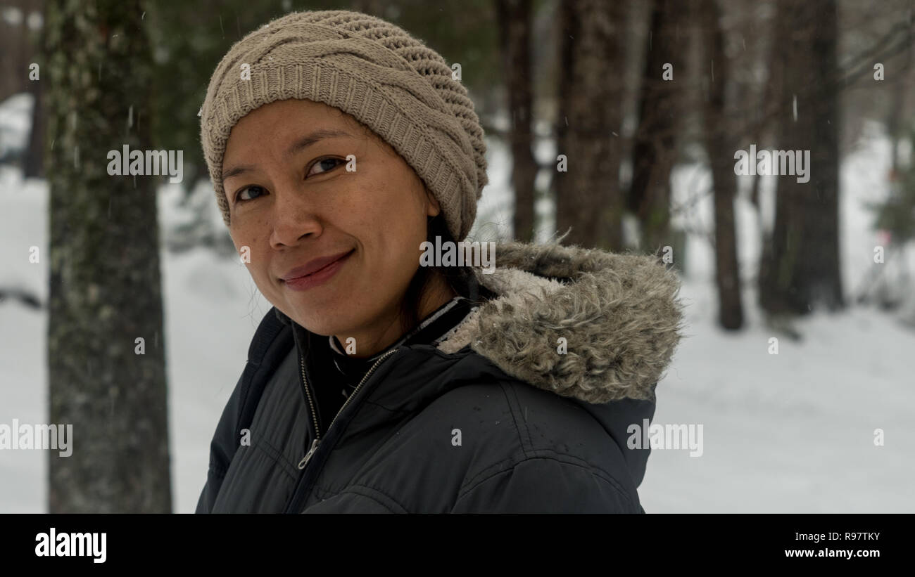 Ritratto di donna asiatica con biege knit hat in piedi nella neve Foto Stock