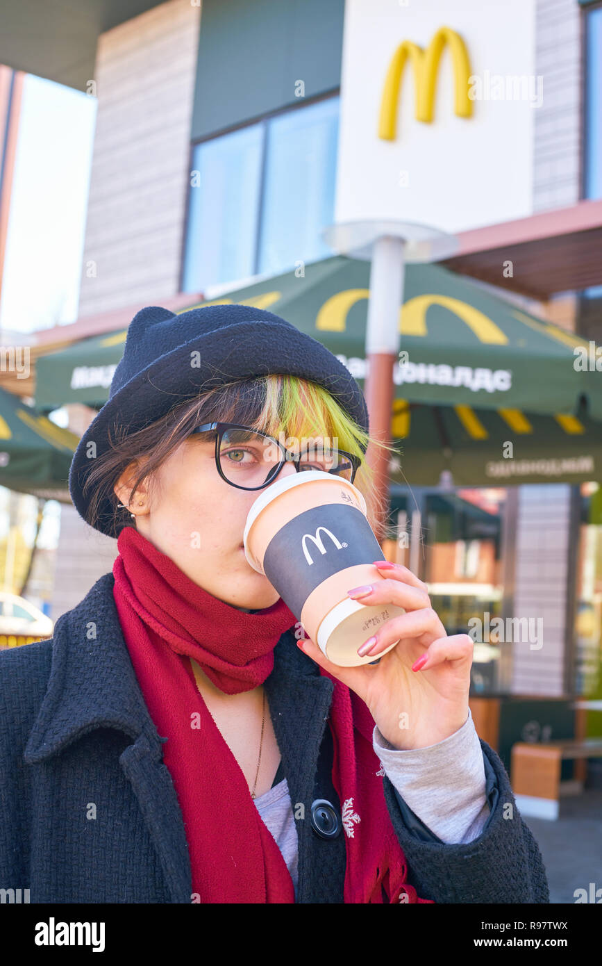 KALININGRAD, RUSSIA - circa aprile, 2018: giovane donna beve un caffè in background del ristorante McDonald's. Foto Stock