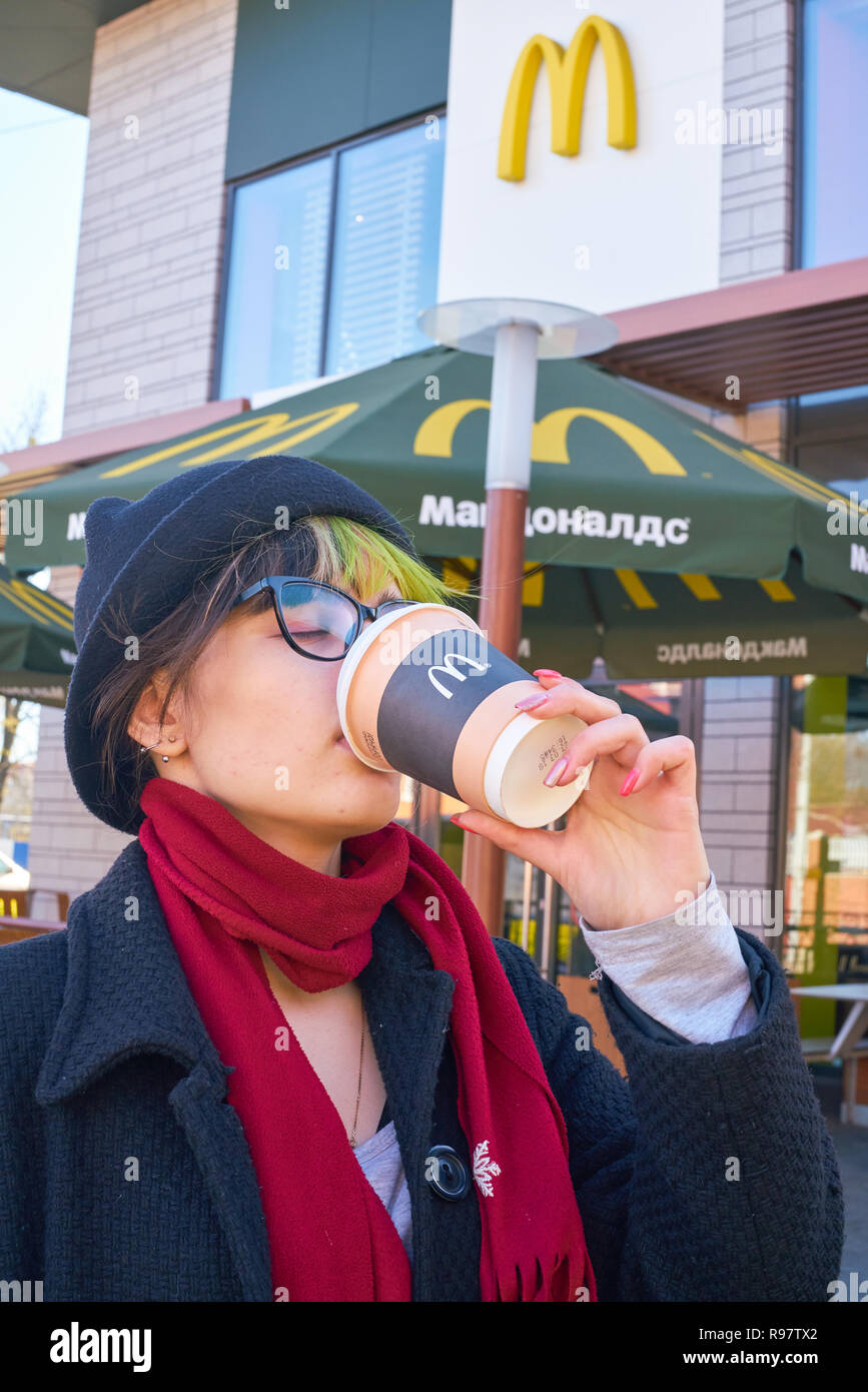 KALININGRAD, RUSSIA - circa aprile, 2018: giovane donna beve un caffè in background del ristorante McDonald's. Foto Stock