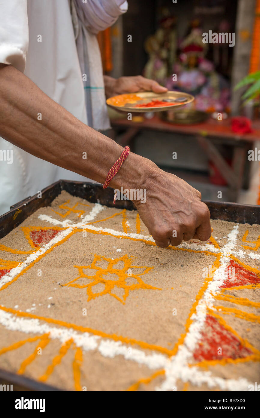 Sacerdote indù la colorazione tradizionale arte di sabbia (Rangoli) con religiosa pattern usando i colori da pigmenti naturali come sindoor, a Haldi (curcuma) Foto Stock