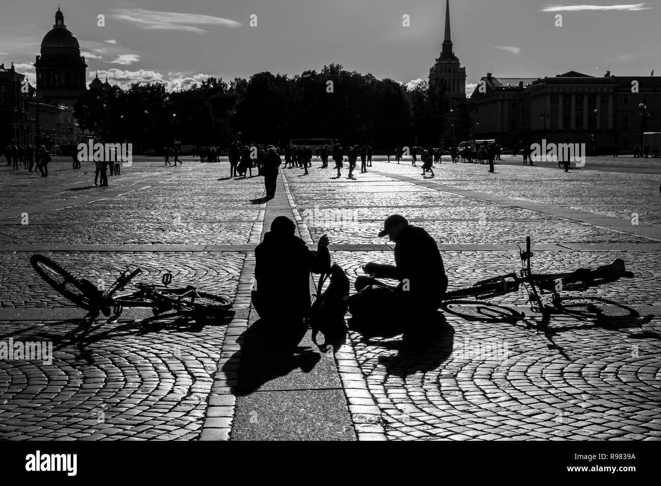 I ciclisti seduto nella Piazza del Palazzo, San Pietroburgo, Russia, accanto a loro bici. Immagine monocromatica shot contre-jour. Foto Stock