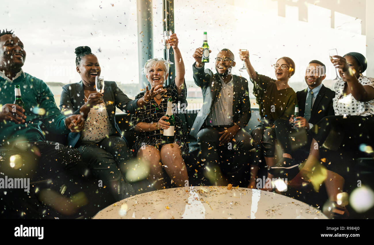 Una festosa multi etnico gruppo di persone sorridenti, tostatura con spumante e birra. Per celebrare la fine dell'anno lavorativo e per il nuovo anno ahe Foto Stock