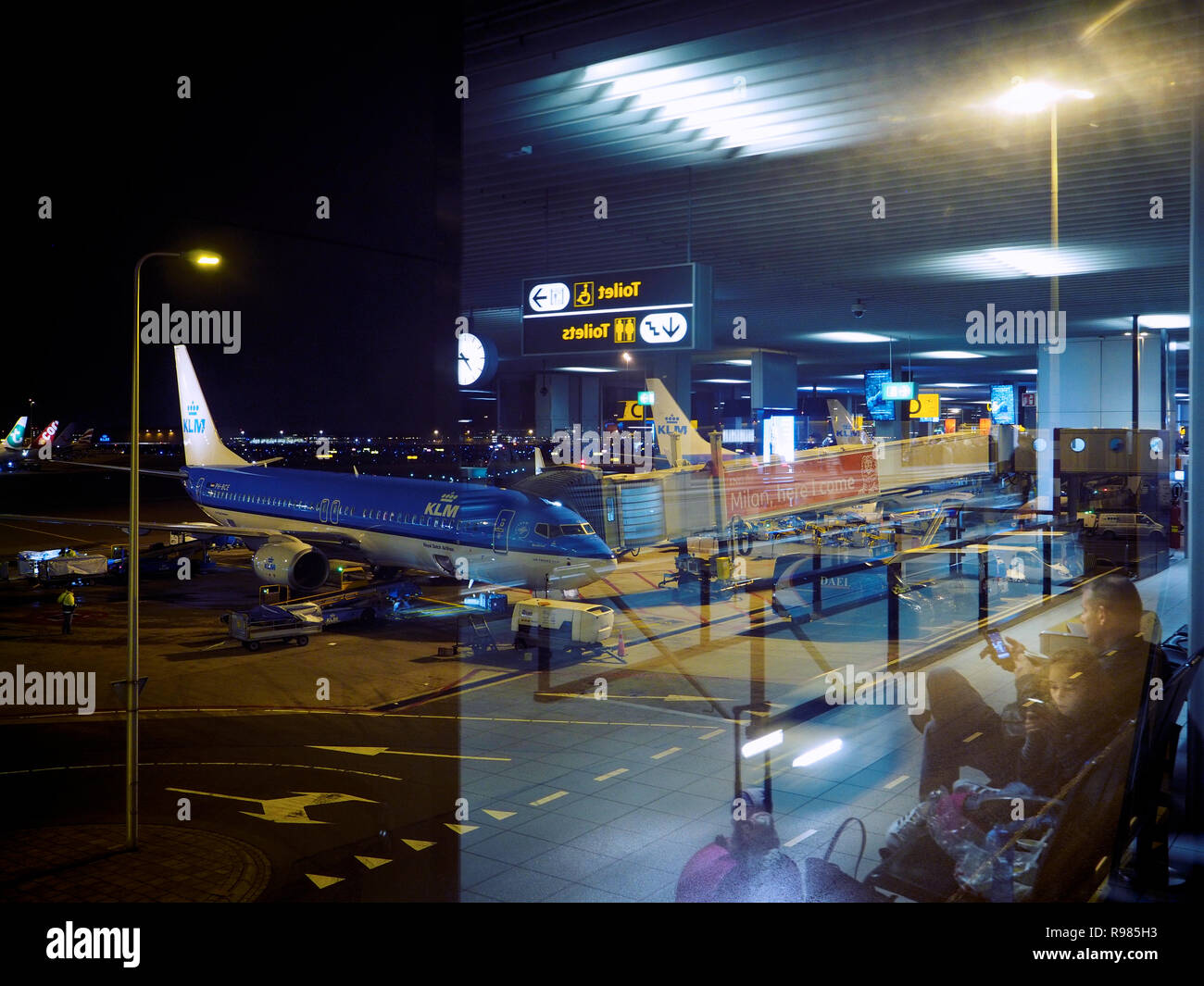 Padre e figlia in attesa all'aeroporto di Amsterdam Schiphol a tarda notte, con KLM Boeing in background. Foto Stock