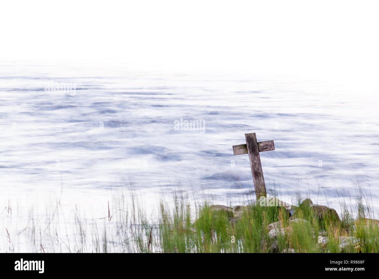 Croce di legno in piedi su un litorale con acqua di streaming in background Foto Stock