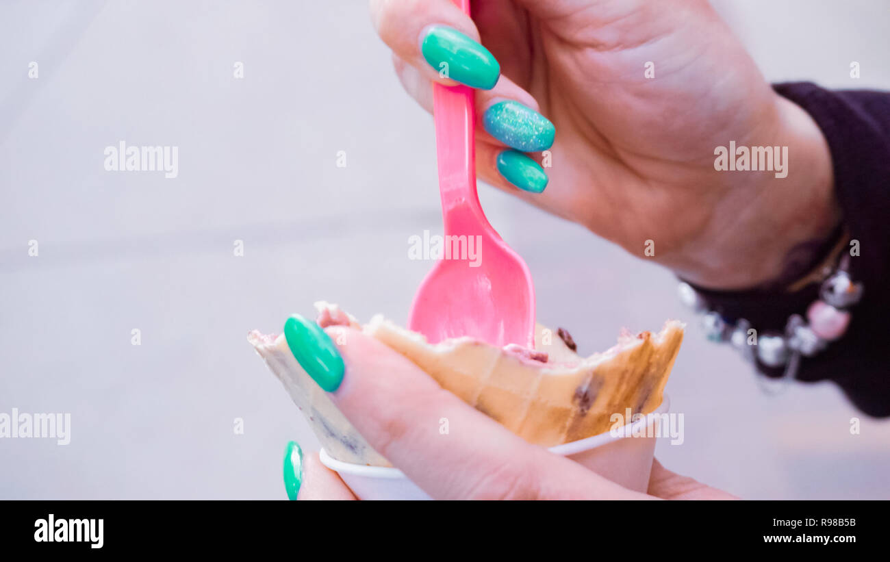 Moman con chiodi blu a mangiare il gelato al di fuori. Foto Stock