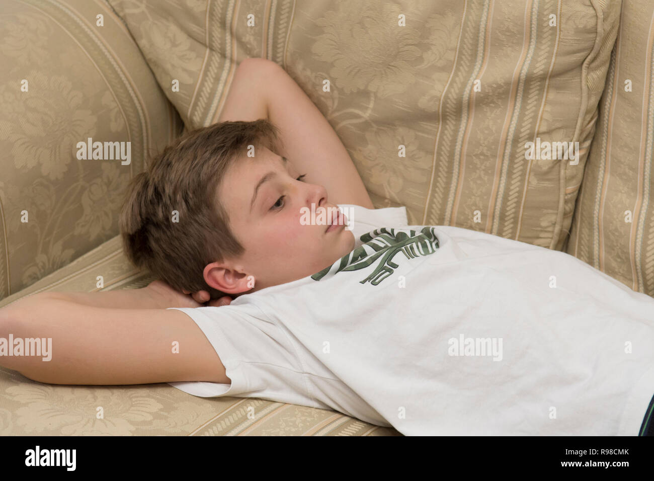 Letargico annoiato sullen moody pigro ragazzo dodicenne che posa su un divano Foto Stock